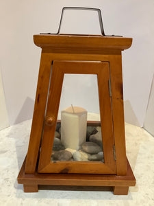 Wooden and glass lantern centrepiece with pillar candle and rocks.