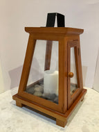 Wooden and glass lantern centrepiece with pillar candle and rocks.